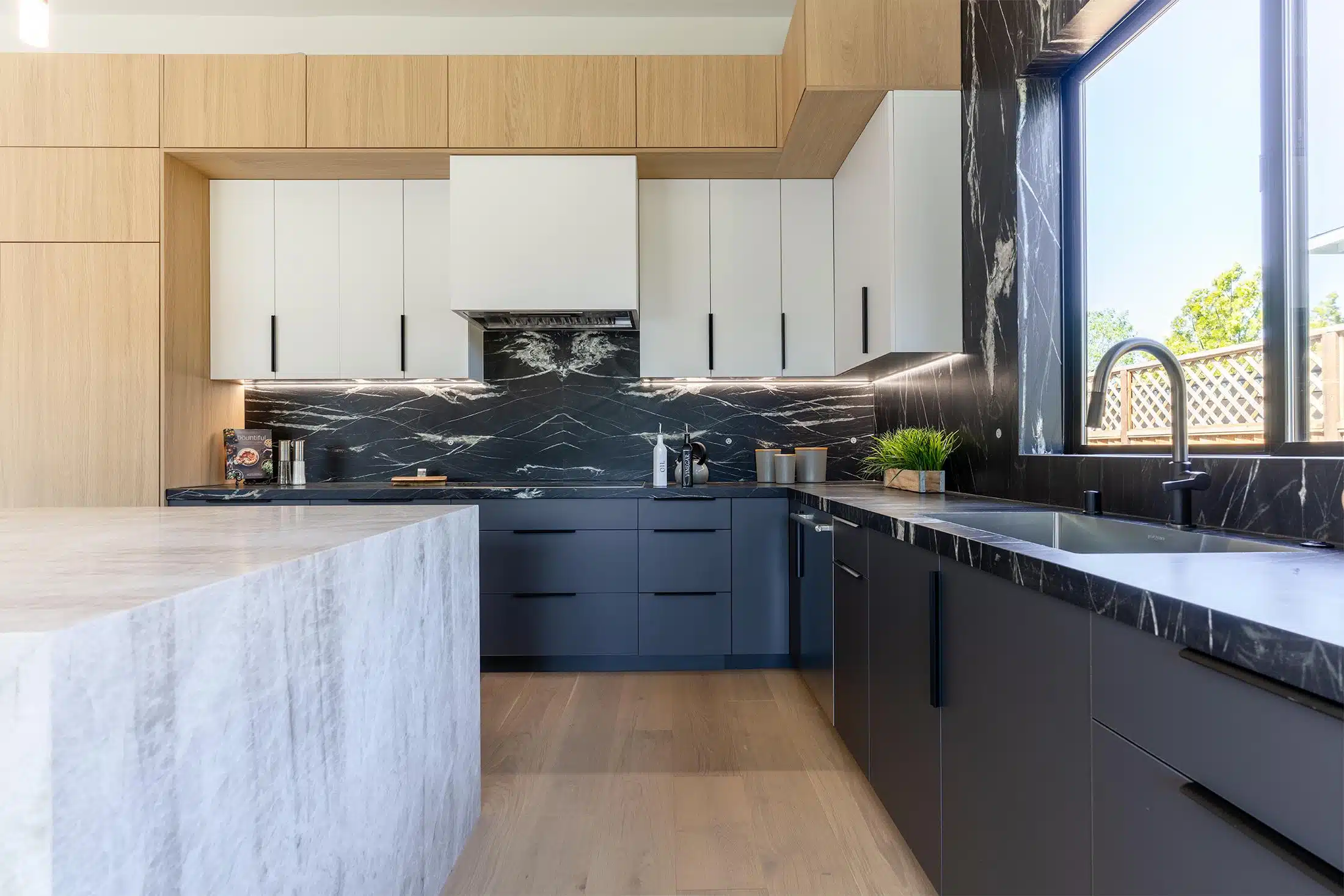 Black marble counter and backsplash beside a travertine island edge